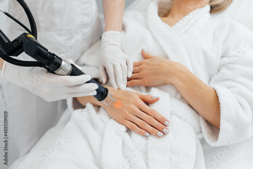 A young girl gets carbon peeling for the skin of her hands in a beauty salon. Laser pulses cleanse the skin. Hardware cosmetology. The process of photothermolysis, warming the skin.