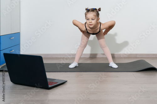 child girl in a gymnastic leotard is engaged in fitness with a trainer online.