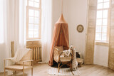 Crib with a cape in a bright bedroom with large windows. Toy giraffe and lounge armchair