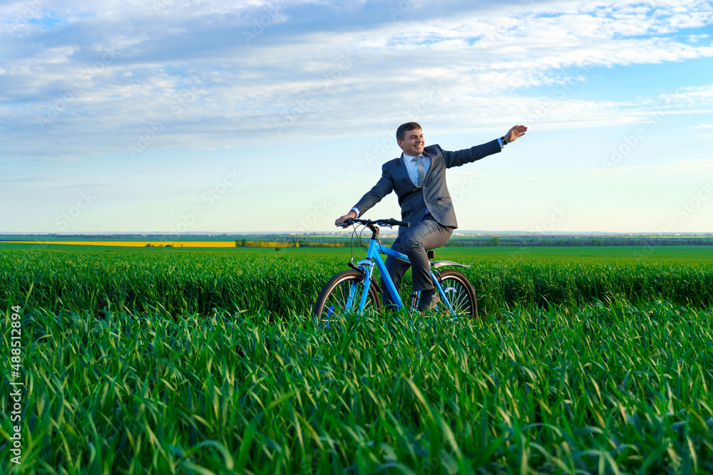 businessman rides a bicycle through a green grass field and waves his hands, dressed in a business suit, beautiful nature in spring, business concept businessman rides a bicycle through a green grass field and waves his hands, dressed in a business suit, beautiful nature in spring, business concept