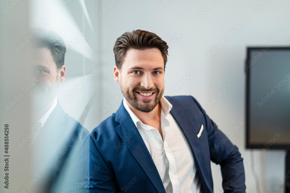 Happy businessman leaning on glass wall in office Happy businessman leaning on glass wall in office
