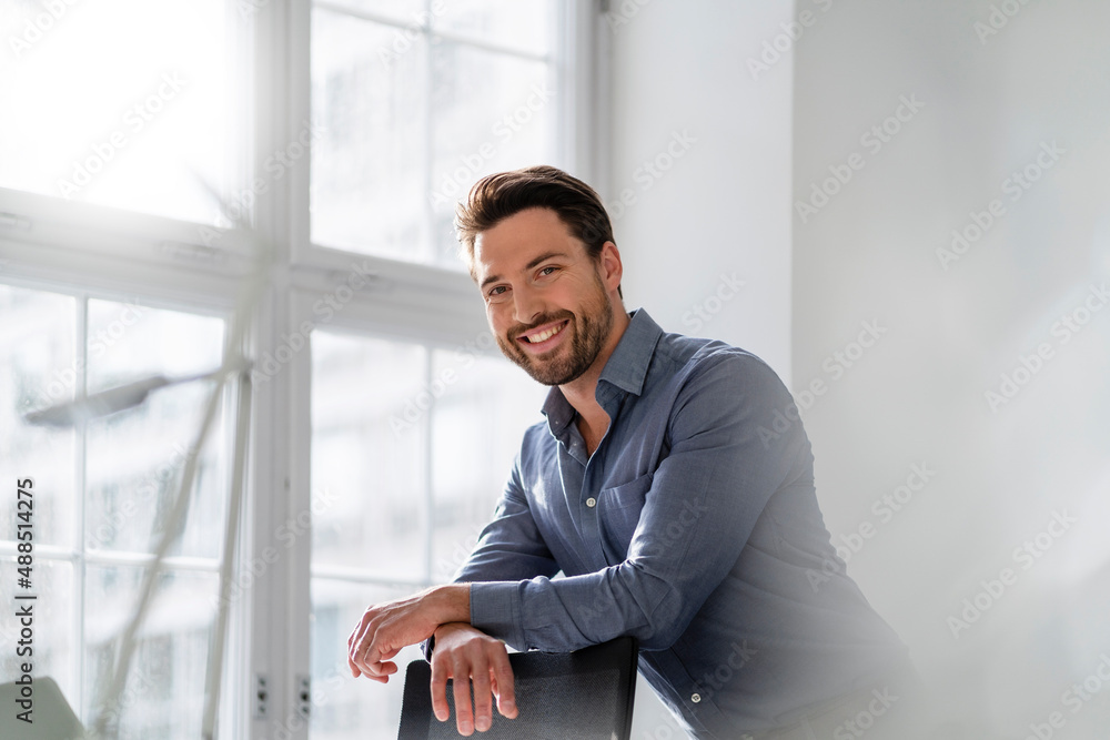 Smiling businessman leaning on chair at office Smiling businessman leaning on chair at office