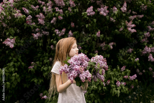 Blond girl with eyes closed holding lilac flowers in nature photo
