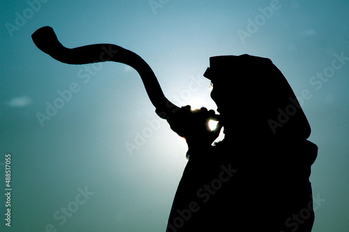 Silhouette of a Jewish man wearing a tallit and blowing a long, curly shofar made from the horn of a kudu antelope at sunrise in Israel. photo