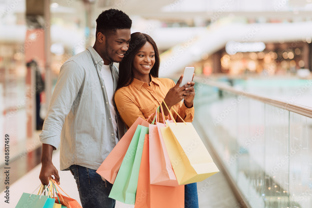 Portrait of excited black spouses using phone in shopping mall Portrait of excited black spouses using phone in shopping mall