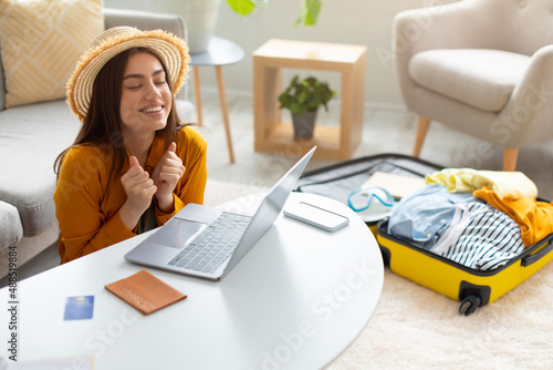 Overjoyed young woman booking hot tour online, excited over sale in tourist agency, using laptop to book hotel from home photo