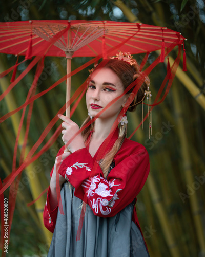 Portrait of a girl in a hanbok with a red umbrella with ribbons