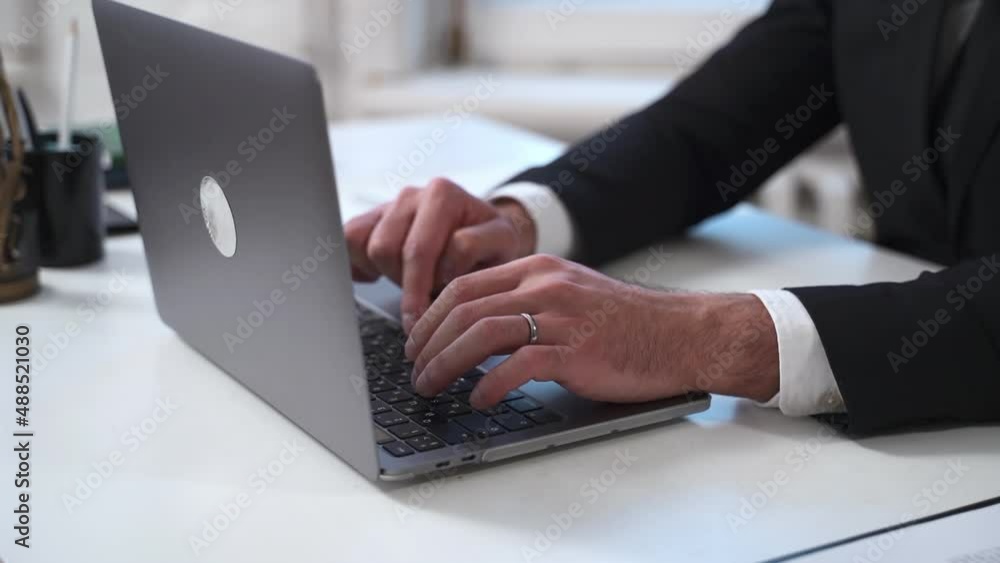 Closeup of young businessman typing on laptop keyboard and sitting at desk in company spbas. American man types text in front of device display and does remote or legal work, sits at table with statue Closeup of young businessman typing on laptop keyboard and sitting at desk in company spbas. American man types text in front of device display and does remote or legal work, sits at table with statue