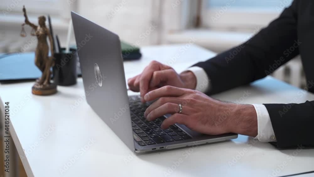 Male professional lawyer typing and working in front of laptop at table in modern office spbas. Close view of young man types text on computer keyboard and does legal work or searches on internet Male professional lawyer typing and working in front of laptop at table in modern office spbas. Close view of young man types text on computer keyboard and does legal work or searches on internet