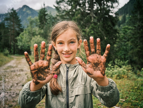 Smiling girl showing muddy hands in forest photo