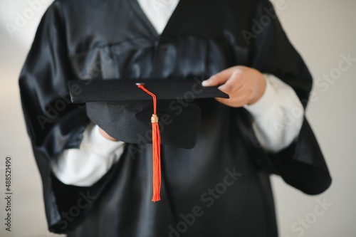 Happy Indian university student in graduation gown and cap holding diploma certificate.