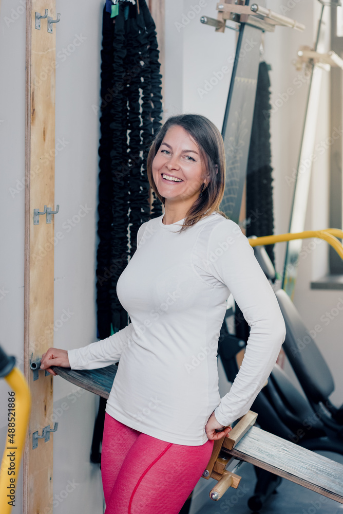 Cheerful muscular middle aged woman in sportswear posing near exercise machine