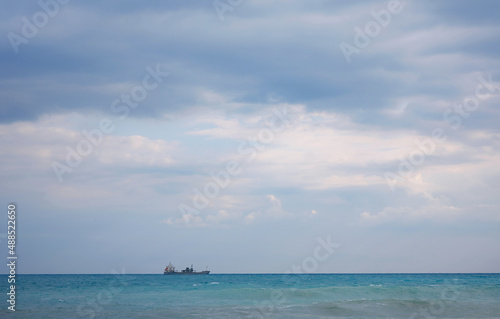 Cargo ship in calm blue Mediterranean in Anatalya. Traveling along the Mediterranean Sea, view of rocky coast of Antalya. In distance, cargo ships are visible. © YURII Seleznov