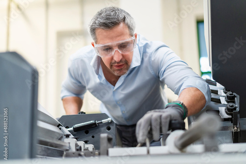 Businessman wearing protective eyewear examining machinery in factory photo