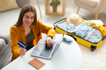 Happy young woman with credit card booking vacation at travel agency or making hotel reservation online, using laptop