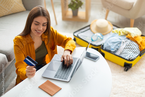 Happy young woman with credit card booking vacation at travel agency or making hotel reservation online, using laptop