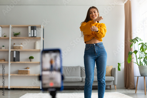 Millennial female lifestyle blogger filming video on cellphone, dancing on webcam at home