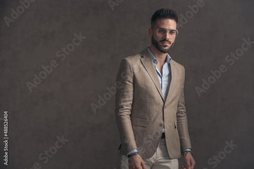 confident bearded man with eyeglasses in beige suit looking away