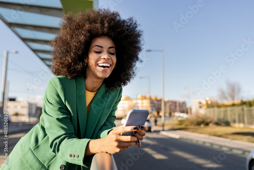 Cheerful commuter using smart phone leaning on railing photo