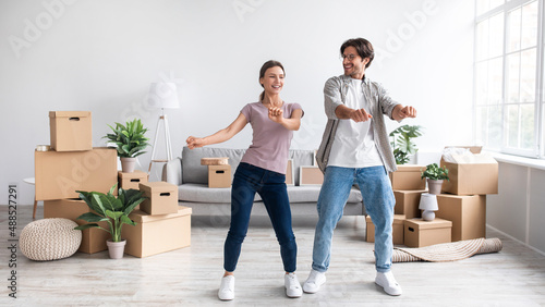 Glad millennial european lady and guy dance, have fun, packing belongings together in room with cardboard boxes