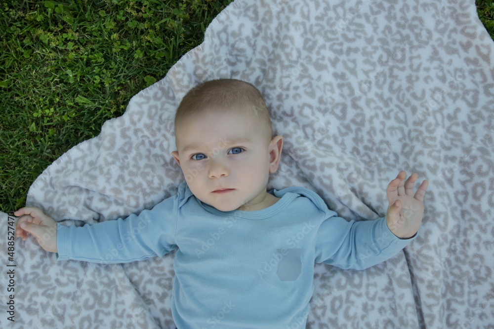 Portrait of cute blue eyed baby boy laying down on the blanket on the grass, top view Portrait of cute blue eyed baby boy laying down on the blanket on the grass, top view