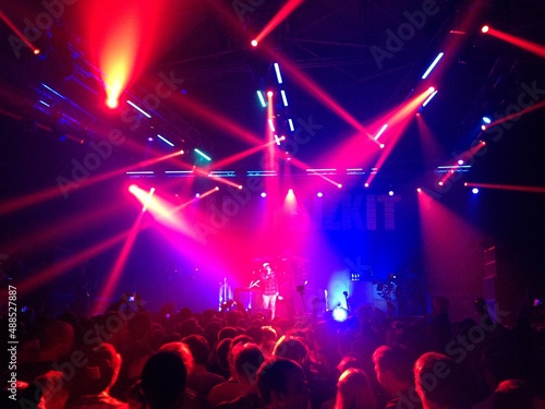 Crowd of fans in front of a stage at a gig. Fans and their favorite band at live performance.  Red lights above the stage. Gig  concert. Strobe lights. Scene. Perform. Musical band