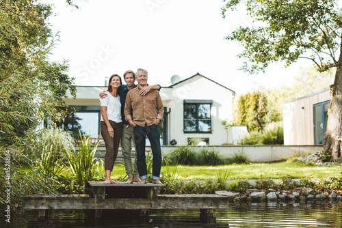 Smiling family standing together on jetty by lake at backyard photo