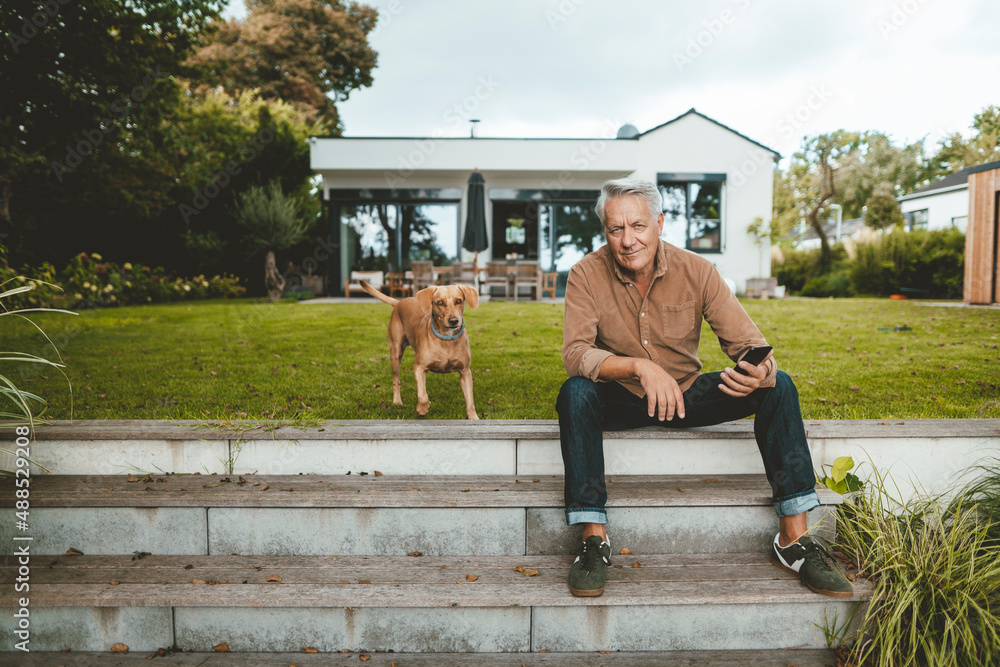 Senior man with smart phone sitting by dog on steps at backyard Senior man with smart phone sitting by dog on steps at backyard