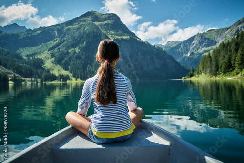 Girl sitting on prow of rowboat and admiring mountains