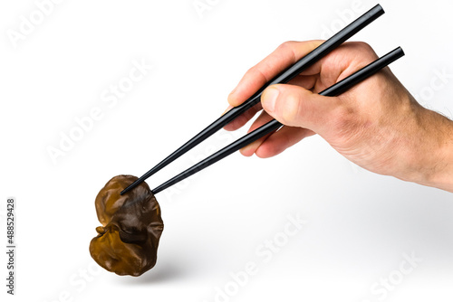Male hand holds chopsticks with ear mushroom. Muer or jew`s ear mushroom taken with chopsticks. Edible dark fungus - auricularia polytricha, also known as cloud ear, black mushroom, jelly fungus