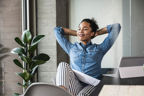 Young businesswoman relaxing with hands behind head in office