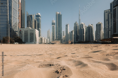 Photography View of sand dunes of desert against backdrop of blurry skyscrapers
