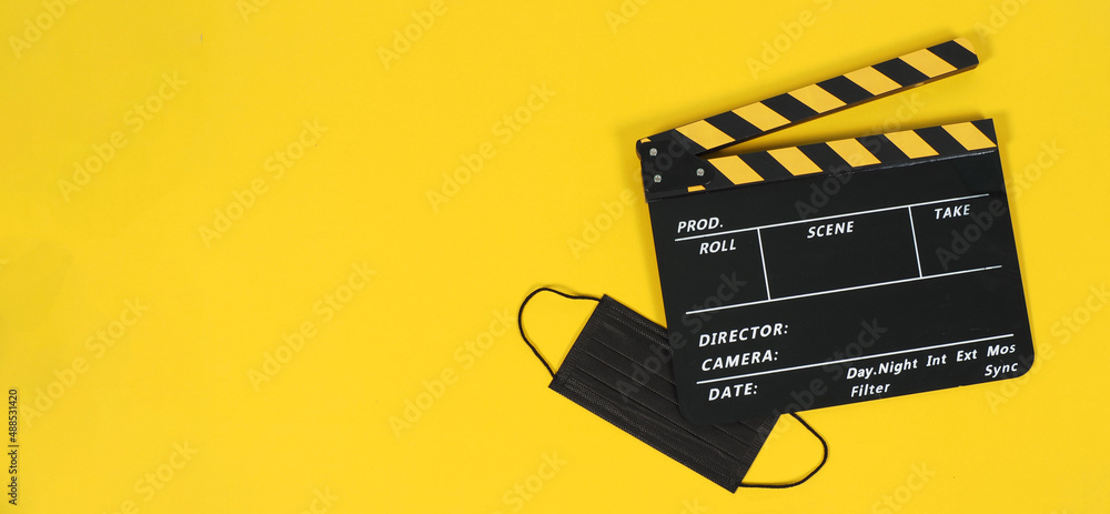 Naklejka premium Black clapper board and black face mask on yellow background.