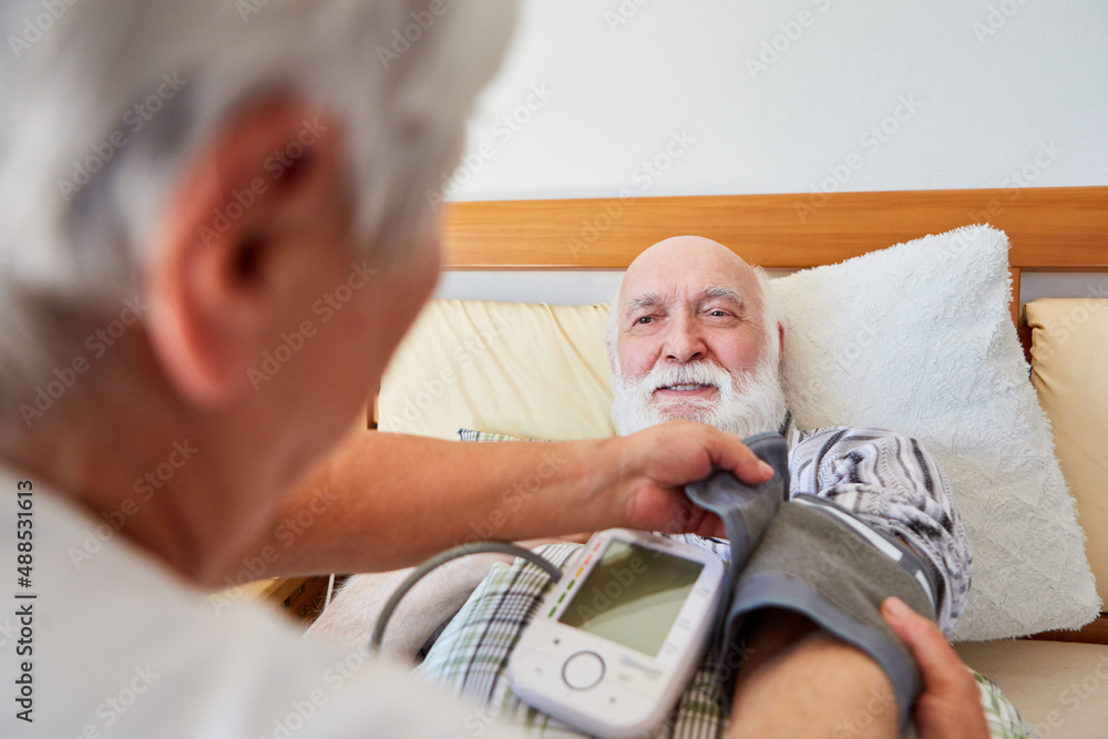Nursing service checks senior's blood pressure in bed Stock Photo