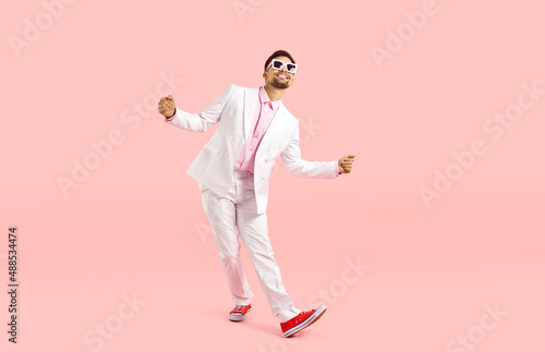 Foto Happy funny guy in white suit dancing isolated on pastel pink background