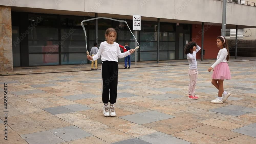 Cheerful sporty tween girl jumping rope in school yard during recess in ...