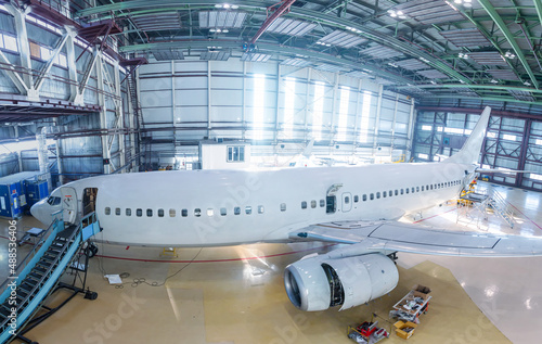 White passenger airliner in the hangar. Airplane under maintenance. Checking mechanical systems for flight operations