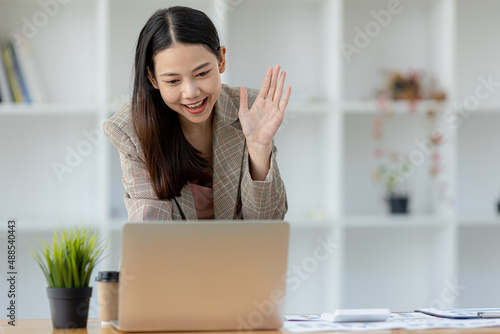 Beautiful Asian businesswoman sitting in her private office, she is talking to her partner via video call on her laptop, she is a female executive of a startup company. Concept of financial management