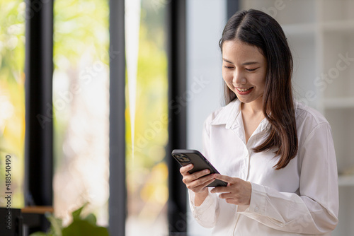 A woman playing a mobile phone by the window  a young businesswoman and a young executive founded a startup that has consistently made high profits. Concept of young businesswoman and startup company.