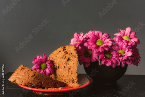 Ciasto piernik na talerzyku, różowe kwiaty, margaretki obok. 