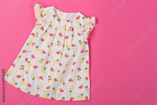 white baby dress with drawings of watermelon and pineapple slices, on a pink background, shopping concept