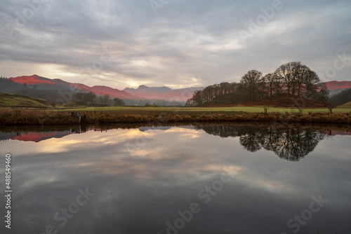 Beautiful morning light on Cumbrian mountains reflecting in calm river on a peaceful morning at The River Brathay in The Lake District, UK. photo