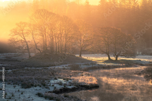 Breathtaking golden light illuminating frosty Winter landscape with misty river near Elterwater in the Lake District, UK.