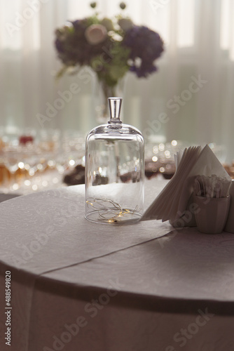 Glowing garland under glass dome on table on table with paper napkins in cafe as Christmas decoration