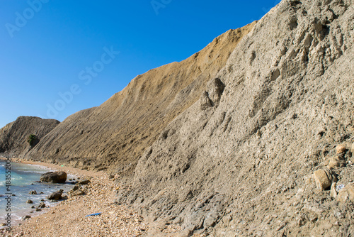 Steep blue clay slopes, with flaking debris forming scree on limestone along the coast of Gozo, in the Maltese Islands, on a beautiful sunny day.
