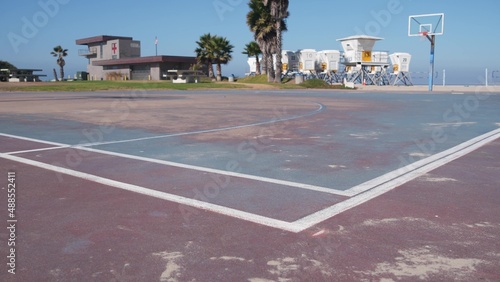 Palm trees and basketball sport field or court on beach, California coast, USA. Streetball playground on shore and lifeguard stand, tower ot station. Mission beach, San Diego. Hoop, backboard and sky.