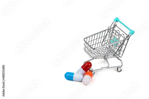 Shopping cart and pills isolated on white background. Three multi-colored capsules. Medico-pharmaceutical concept. Copy space.