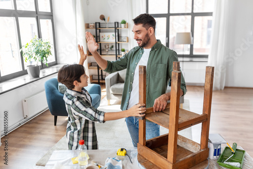 family, diy and home improvement concept - happy smiling father and son restoring old table and making high five gesture at home