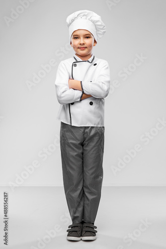 cooking, culinary and profession concept - happy smiling little boy in chef's toque and jacket over grey background