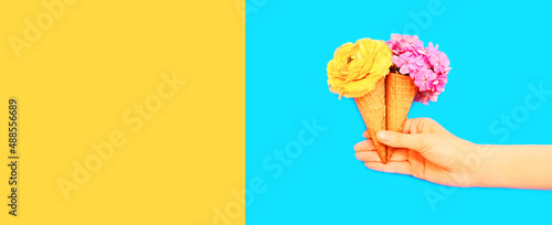 Hand holding cone ice cream with flowers on blue background  blank copy space for advertising text